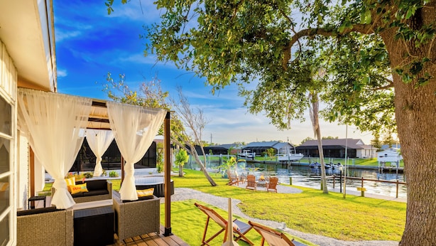A patio with outdoor seating, a view of a water body, and a tree.