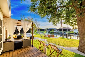 A patio with outdoor seating, a view of a water body, and a tree.