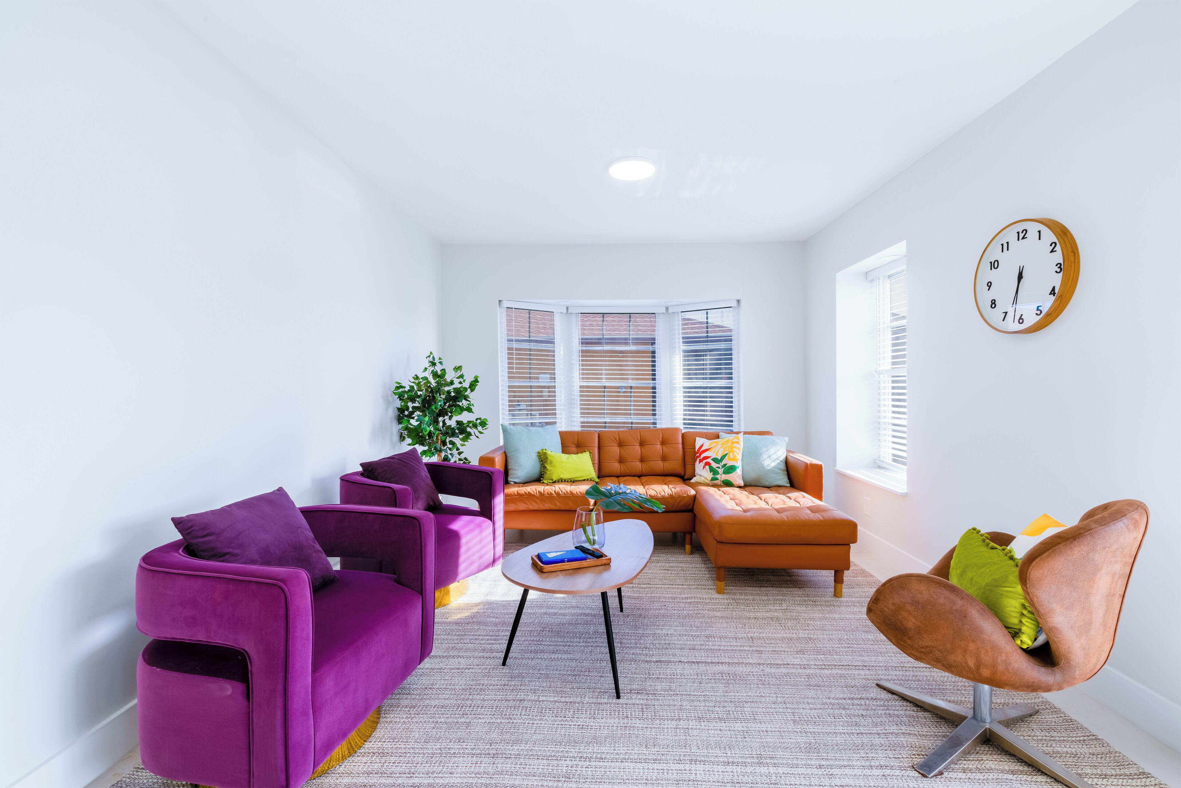 A modern living room with a purple sofa, a brown armchair, and a beige coffee table.