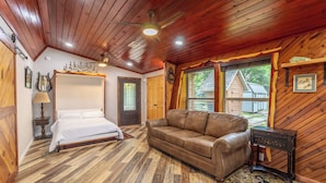Une chambre avec un plancher en bois, un lit à baldaquin, un canapé en cuir et une petite table d’appoint.