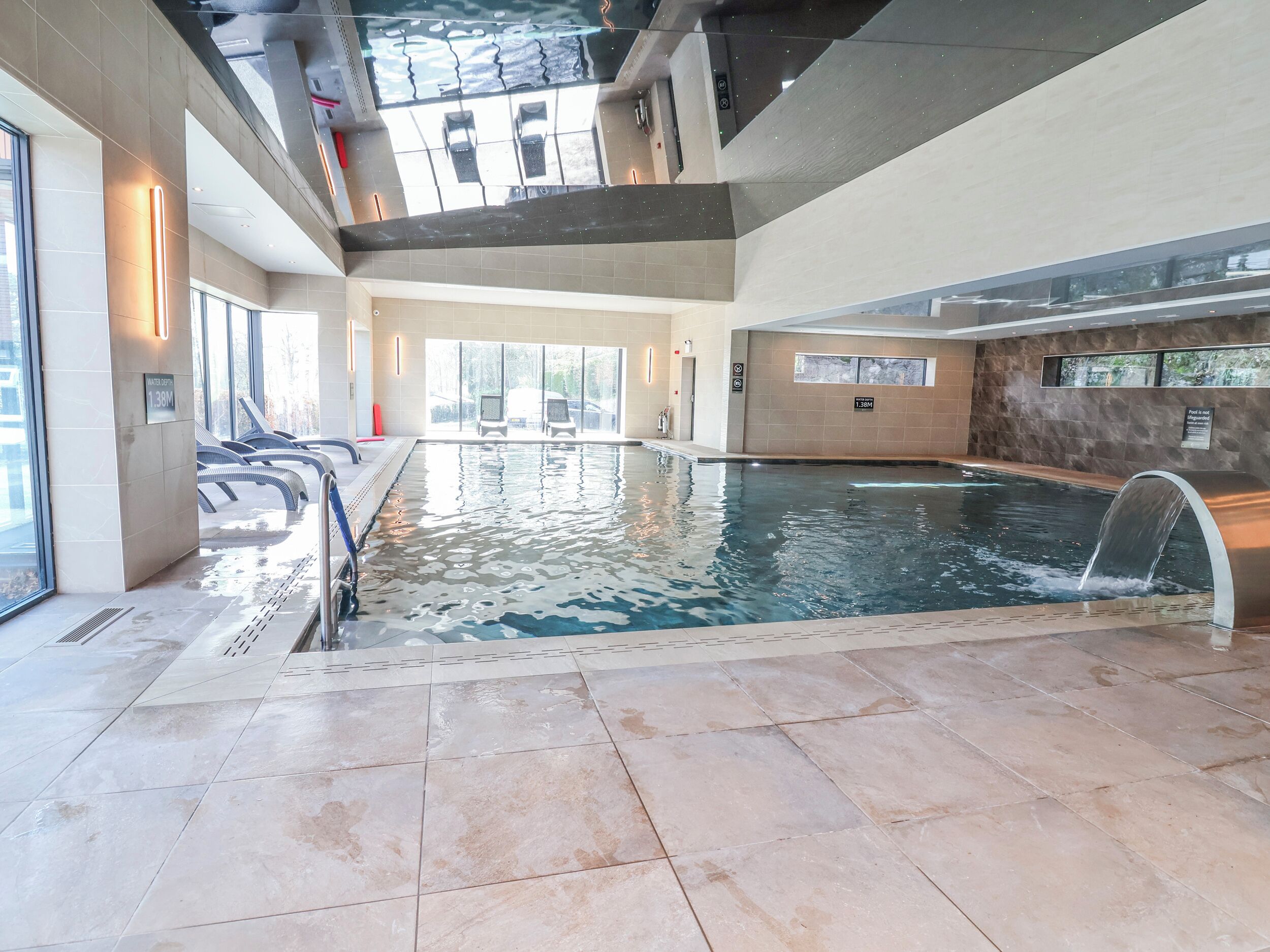 An indoor swimming pool with clear water, a diving board, and lounge chairs.