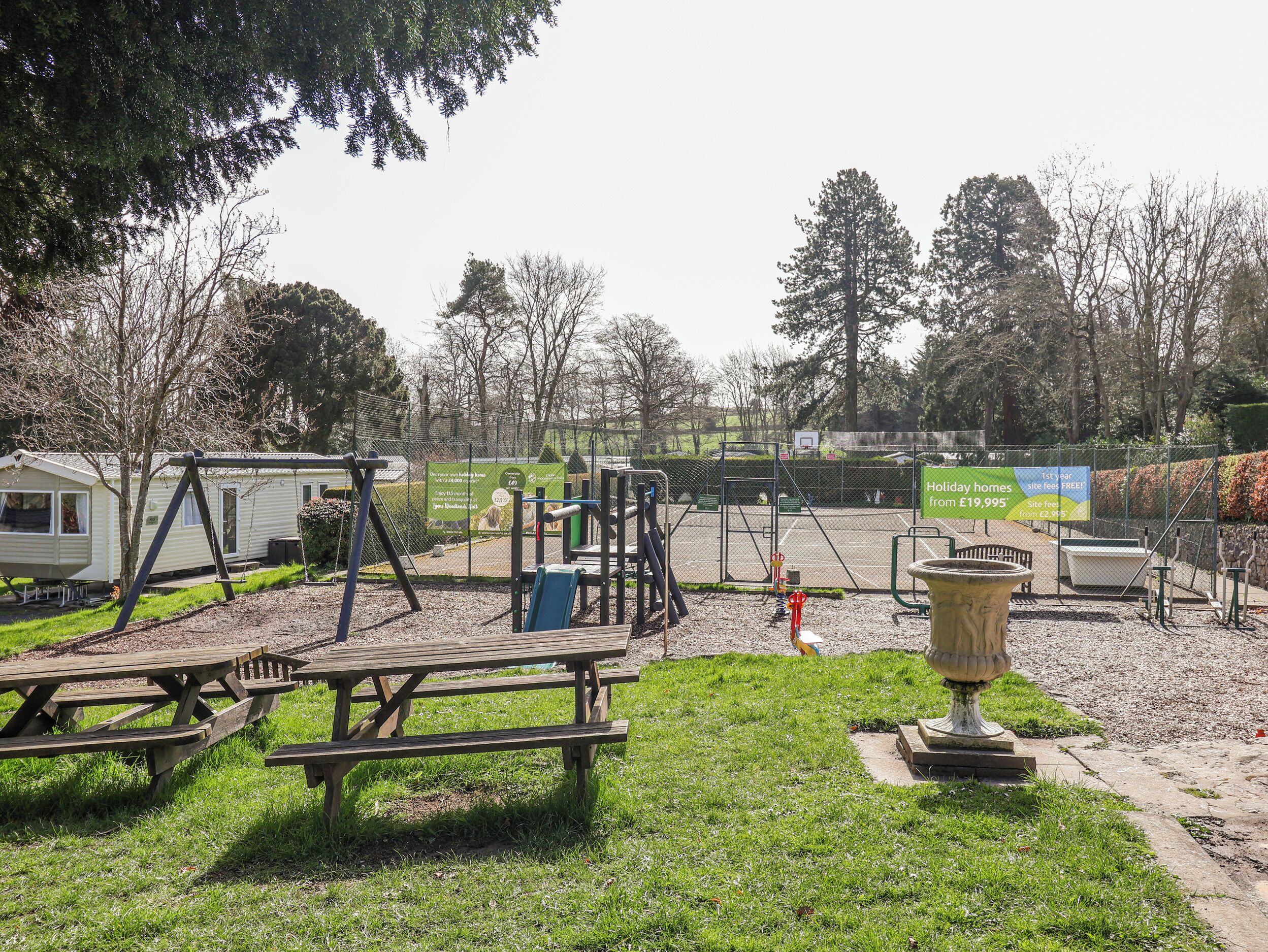 A park with picnic tables, a swing set, a basketball court, and holiday homes.