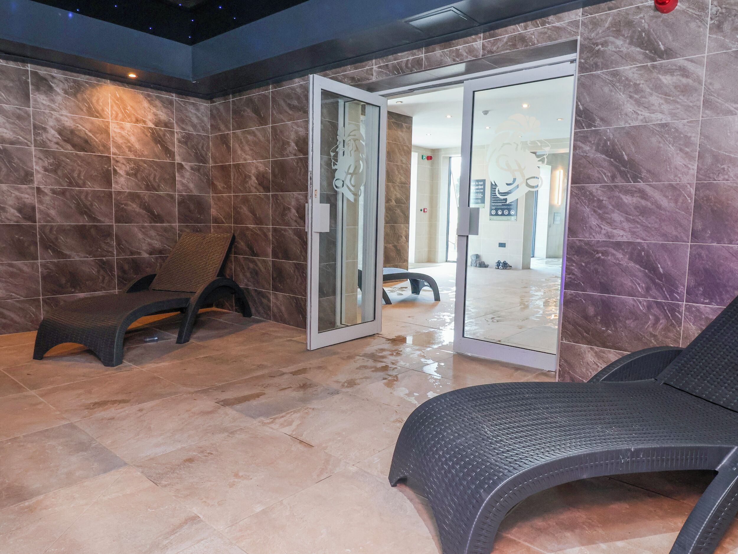 A spa area with a bench, a glass door entrance, and a tiled floor.