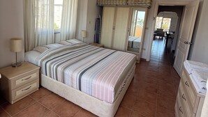 Une chambre à coucher avec un grand lit, une table de chevet, une commode et une fenêtre avec des rideaux.