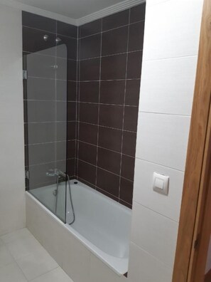 A bathroom with a glass shower enclosure and a white bathtub.