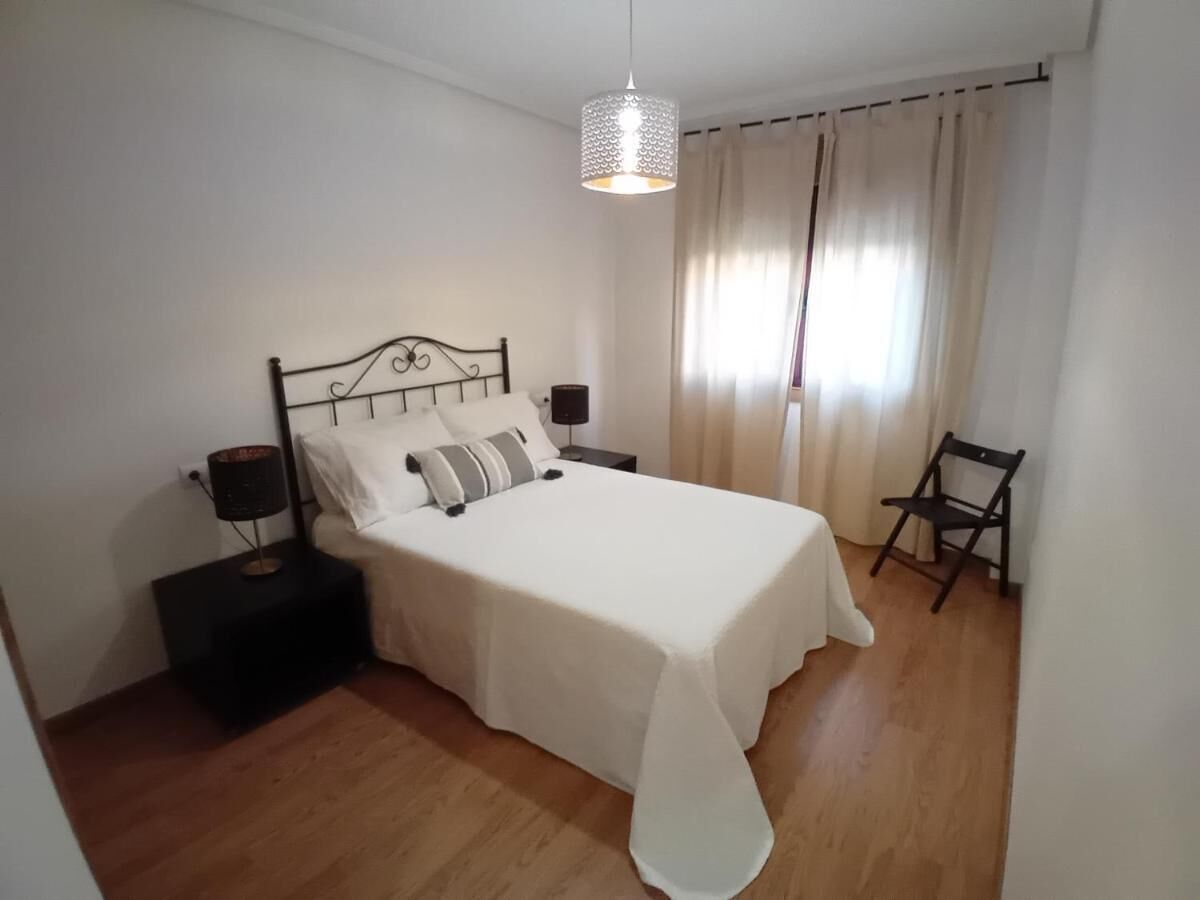 Ein Schlafzimmer mit einem Bett, Nachttischen, einem Sessel und einer Pendelleuchte.