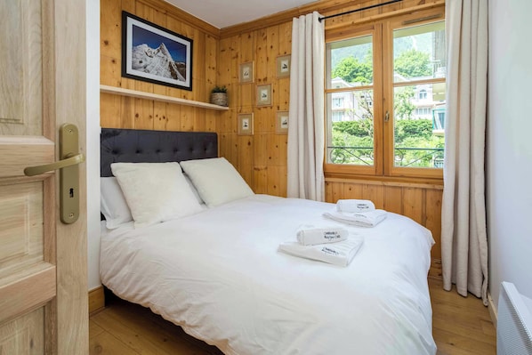 Un dormitorio con cama, almohadas, ventana con cortinas, cabecera de madera y un cuadro enmarcado en la pared.