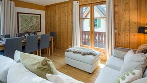 A cozy room with a wooden interior, a dining area with chairs, a sofa, and a window with curtains.