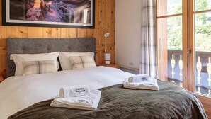 A hotel room with a wooden paneled wall, a large framed picture of a mountain, a bed with white linens, and a window with a view of greenery.