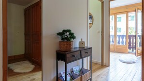 A hallway with wooden flooring, a dark wooden console table with magazines, a small potted tree, and a fluffy white rug.
