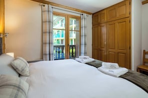 Habitación de hotel con cama, armario de madera y balcón con vista a edificios.