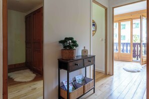 Un pasillo con una puerta de madera, una mesita con una planta y una cesta de mimbre.
