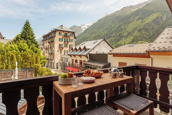 A balcony with a table set for breakfast, overlooking a mountainous landscape with traditional buildings.