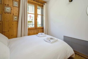Una habitación de hotel con una cama, un ventanal con cortinas, vistas al balcón y cuadros en la pared.
