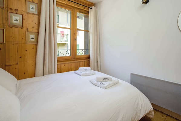 A hotel room with a bed, a window with curtains, a balcony view, and framed pictures on the wall.
