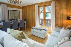 Una habitación acogedora con detalles de madera, un área de comedor con sillas y una mesa, y un ventanal con vistas.