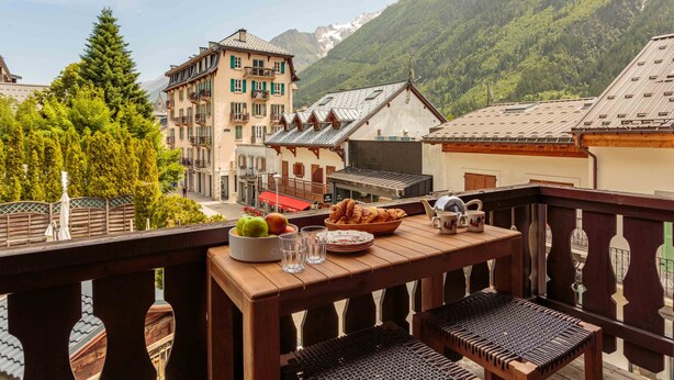 A balcony with a table set for breakfast, overlooking a mountainous landscape with traditional buildings.