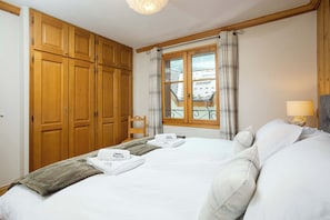 Habitación de hotel con una cama grande, armario de madera y ventana con vistas al tejado.