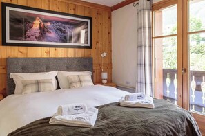 Habitación de hotel con una cama grande, cabecera, mesita de noche, lámpara y ventana con cortinas.