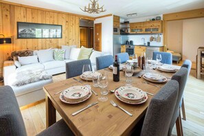 Un interior acogedor con una mesa de comedor para seis personas, una zona de cocina y un espacio de sala de estar con un sofá e imagen colgada.
