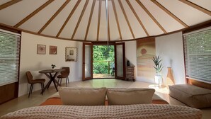 Ein gemütliches Zimmer mit einem Bett, einem Tisch und Stühlen. Ein großes Fenster und eine Tür führen nach draußen.