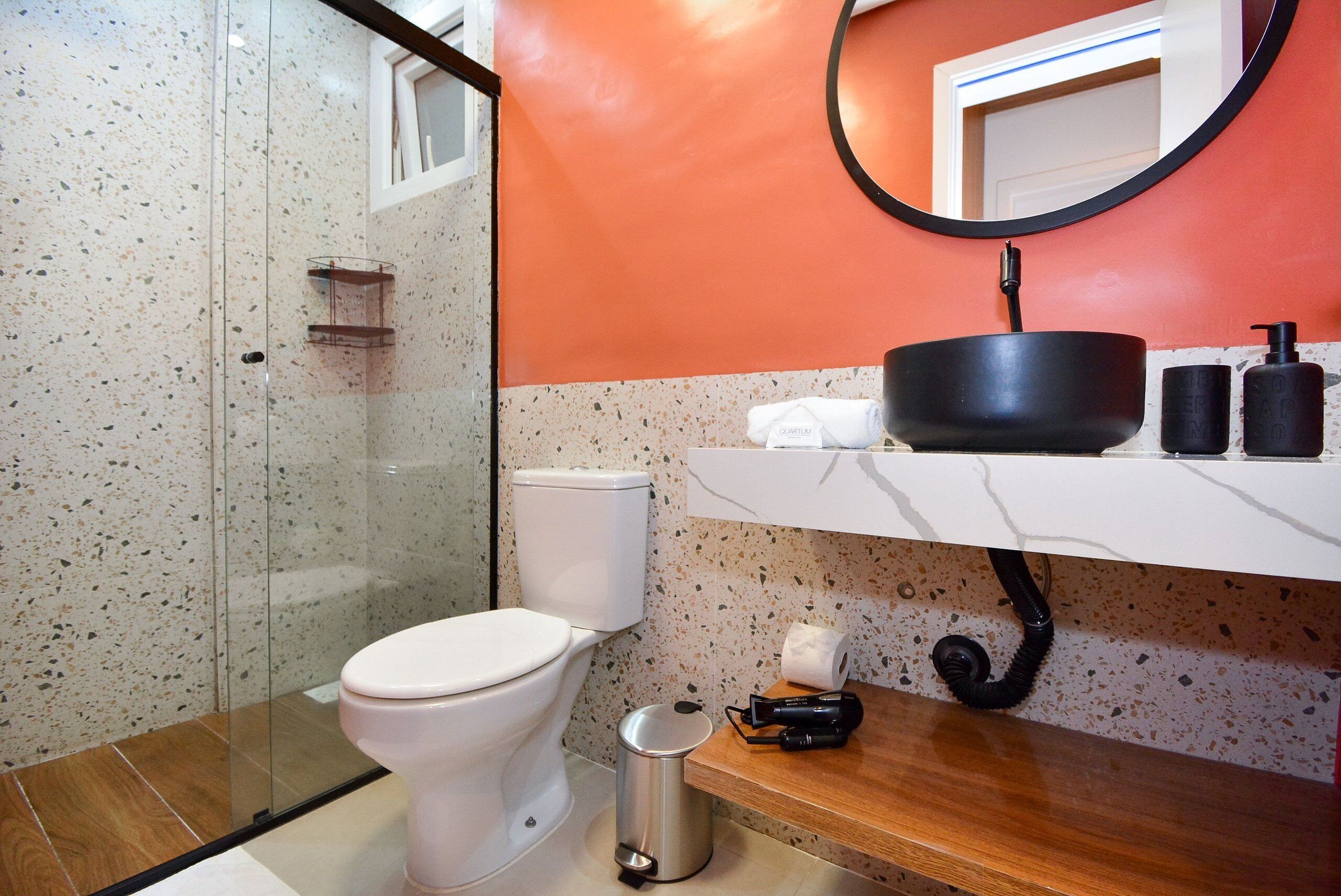 A bathroom with a white toilet, a glass shower enclosure, a wooden vanity with a black sink, and a mirror above the sink.