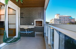 Un balcon avec un fauteuil suspendu, une petite table et un évier encastré.