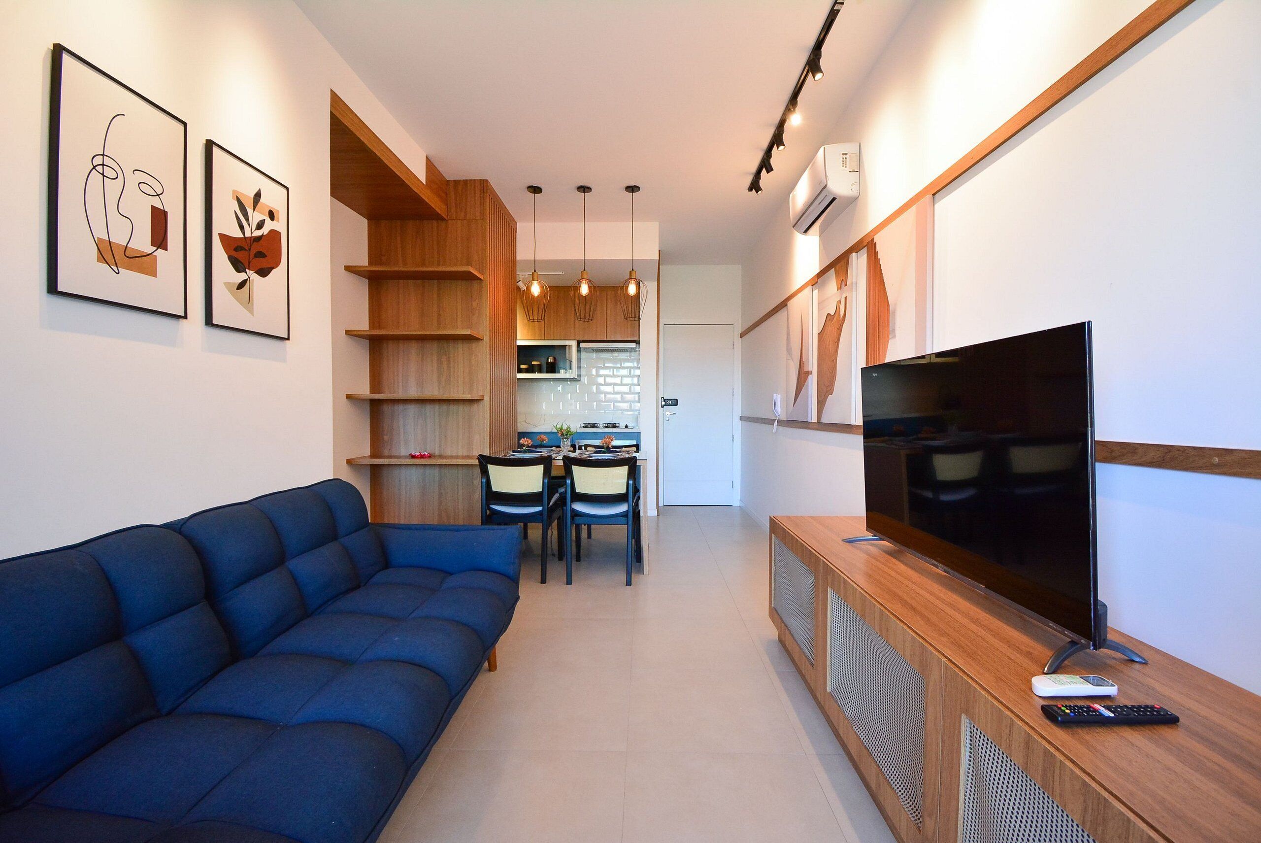 A modern living room with a blue sofa, a wooden entertainment unit with a TV, and a dining area with chairs and a table.