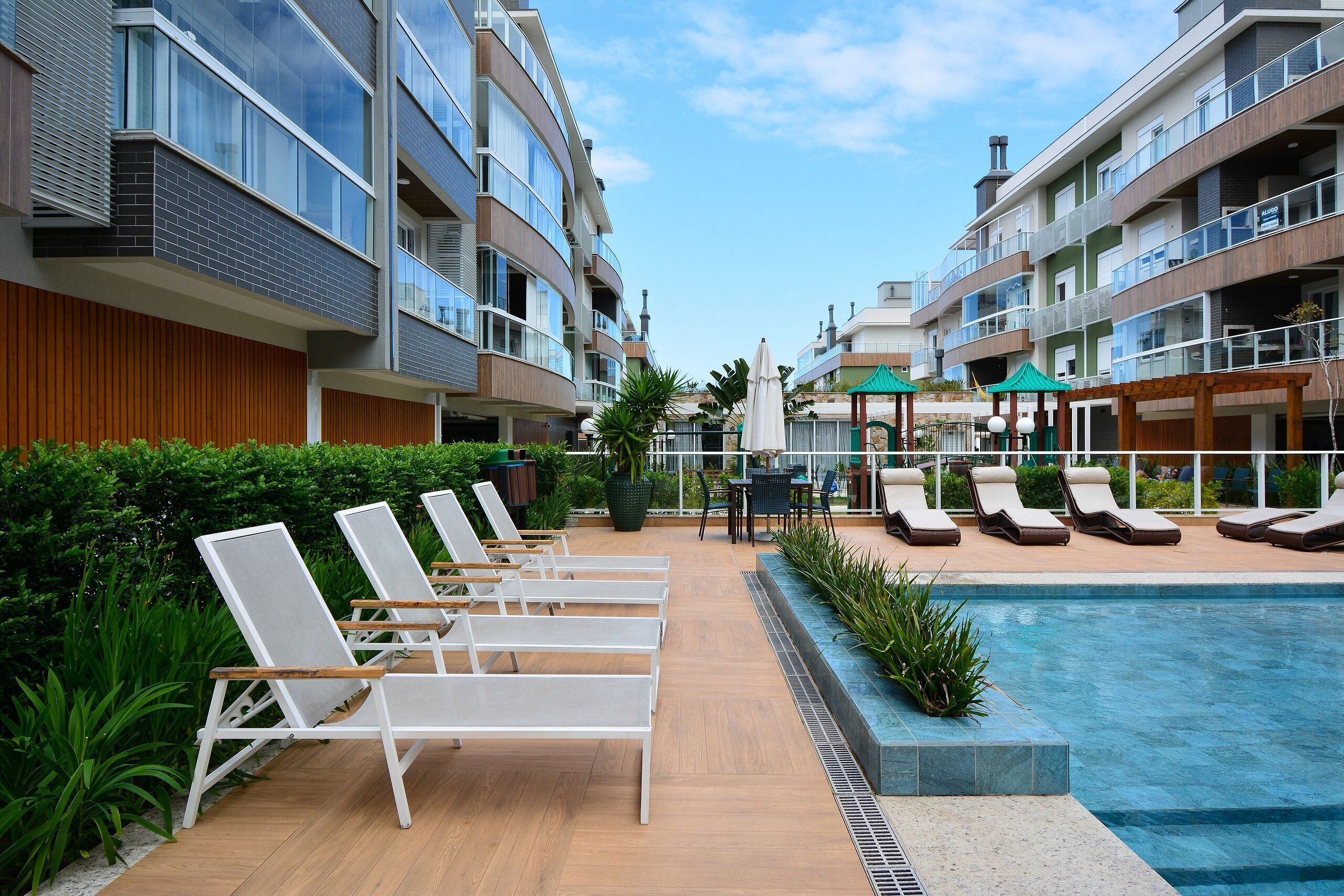A poolside area with sun loungers and a pool, surrounded by multi-story buildings with balconies and large windows.