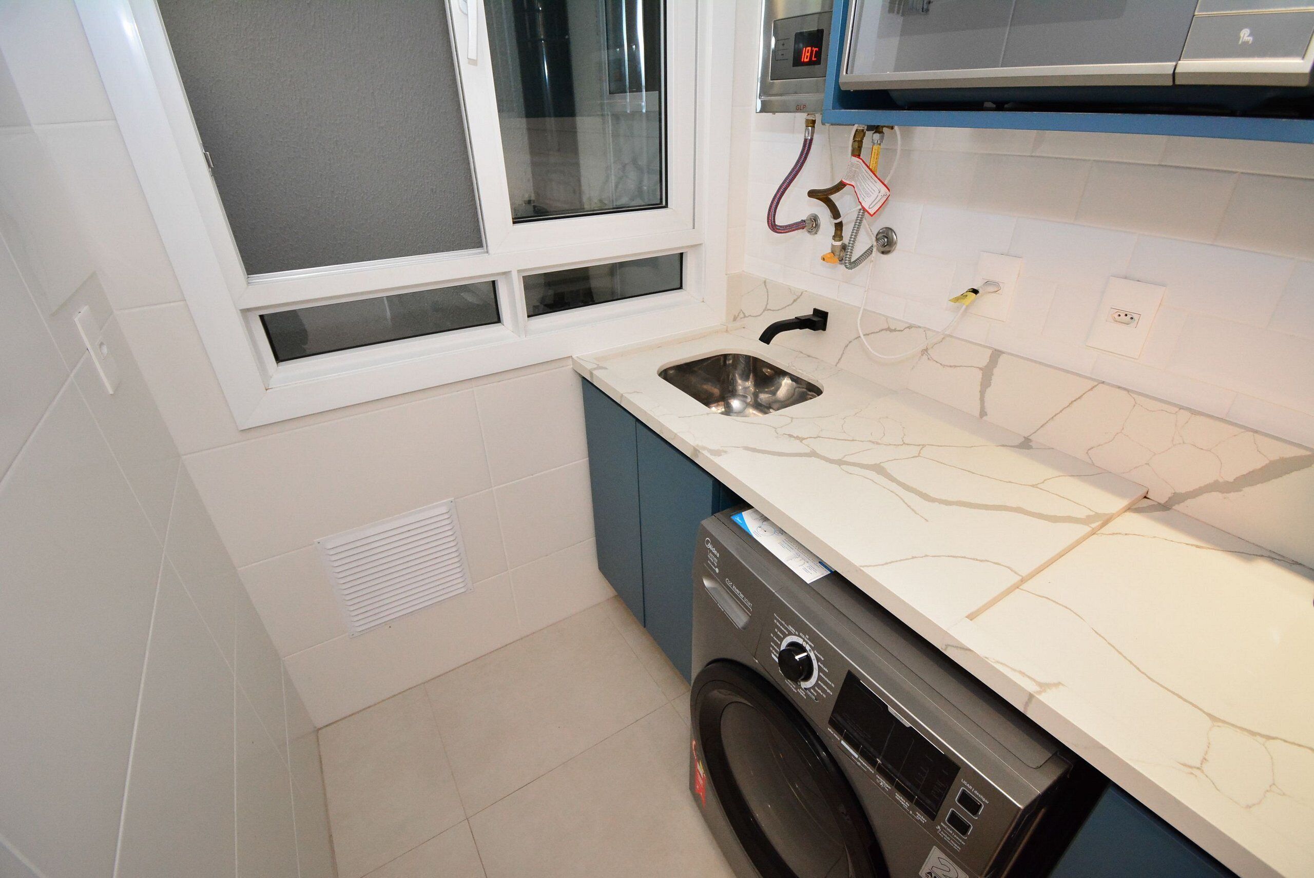A compact kitchen with a built-in washing machine, a window with blinds, and a modern countertop.