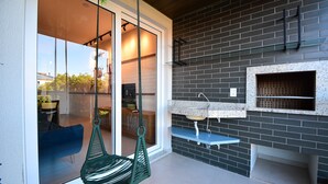 Egy modern konyha, melynek a hátfalát téglaburkolat borítja, van benne egy függő szék, és egy üvegajtó vezet belőle az étkezőbe.