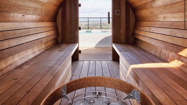 A sauna with wooden walls and benches, a view of a pool, and a clear sky. - Luxury penthouse in enchanting Denver with bar, gym, pool, sauna & more (Denver)
