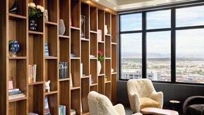 A modern library with a large wooden bookshelf, comfortable seating, and a large window offering a city view. - Luxury penthouse in enchanting Denver with bar, gym, pool, sauna & more (Denver)