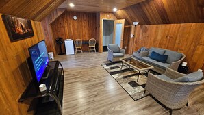 A cozy, wooden-floored living room with a television, wicker furniture, and a dining area with chairs and a table. - Cabin Style Private Studio  (Giroux)