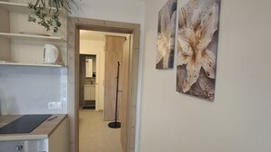 A modern kitchen with a countertop, a coffee maker, and a plant. There is a hallway leading to a bathroom with a mirror and cabinets.