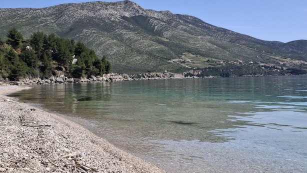 A clear view of a lake with a rocky shoreline and a mountain in the background.