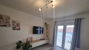 A modern living room with a flat-screen TV, a wooden coffee table, a sofa, and a sliding glass door leading to a balcony.
