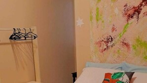 A neatly made bed with a green blanket, a rolled white towel, and a pillow with a leaf pattern. There is a small shelf with a white towel and a star decoration. - Pousada Cabocla (Santarém)