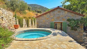 Um edifício de pedra com piscina, cercado por vegetação e um cenário montanhoso.