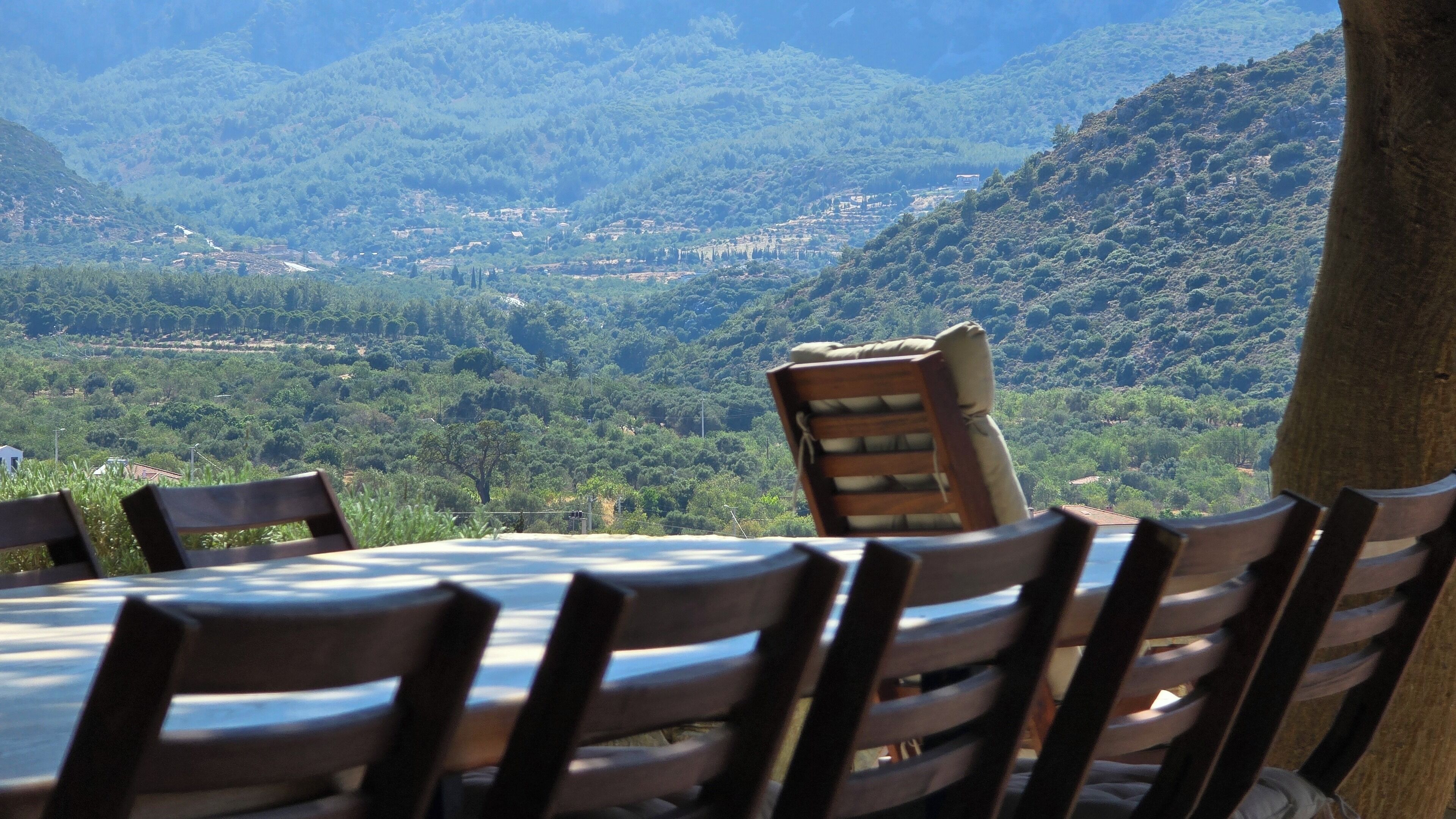 A table with chairs set outdoors, overlooking a mountainous landscape with a village in the valley below.