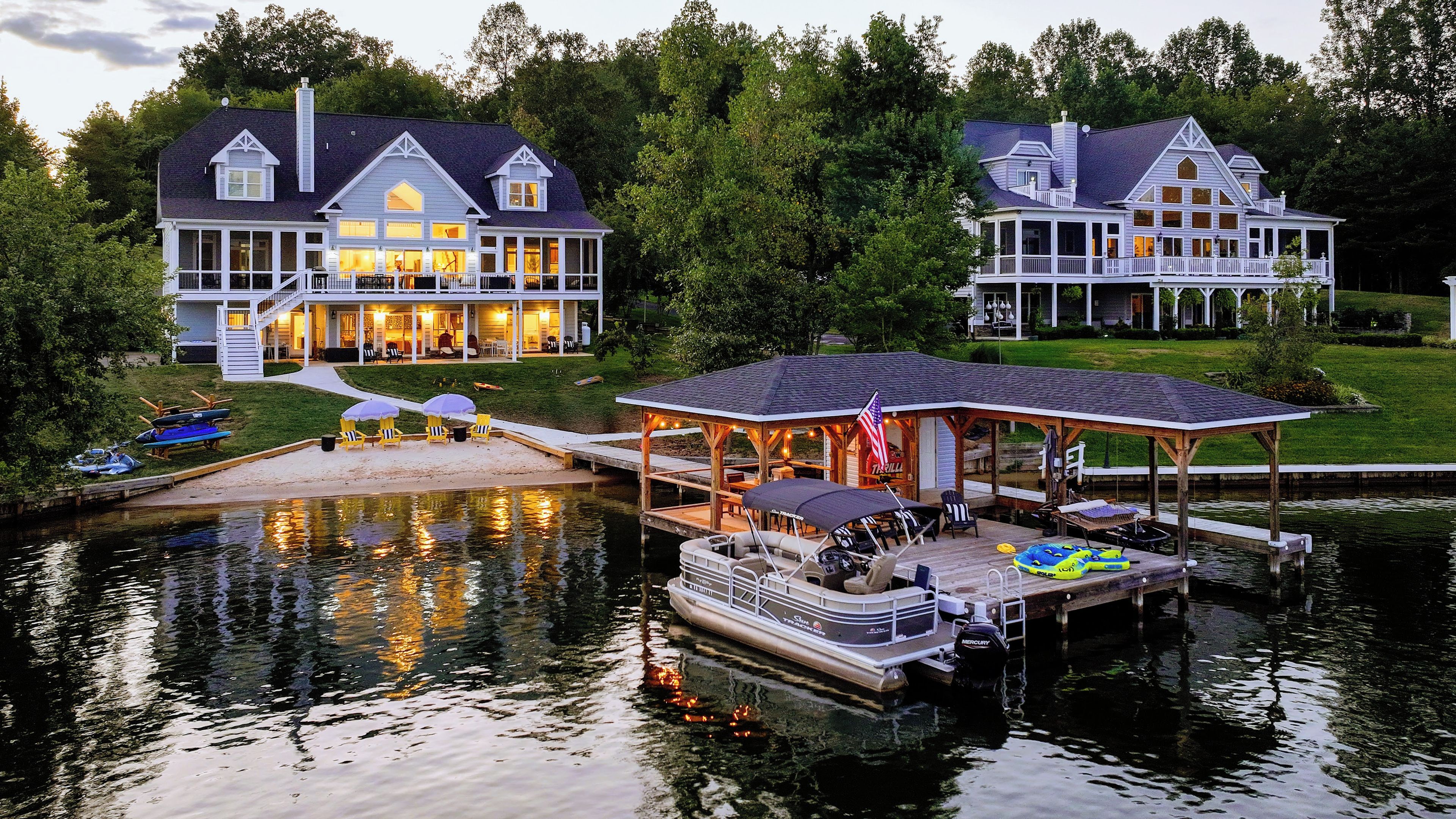 A waterfront property with a dock, a covered boat launch area, and a large house with multiple windows and a porch.