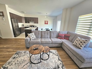 A modern living room with a sectional sofa, a coffee table, and a kitchen in the background.