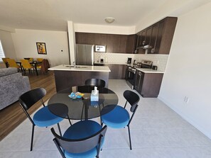 A modern kitchen with dark cabinets, a central island, and a dining area with blue chairs.