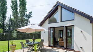 Une maison moderne dotée d’un patio comprenant une table et des chaises, un pot de fleurs et un grand parasol.