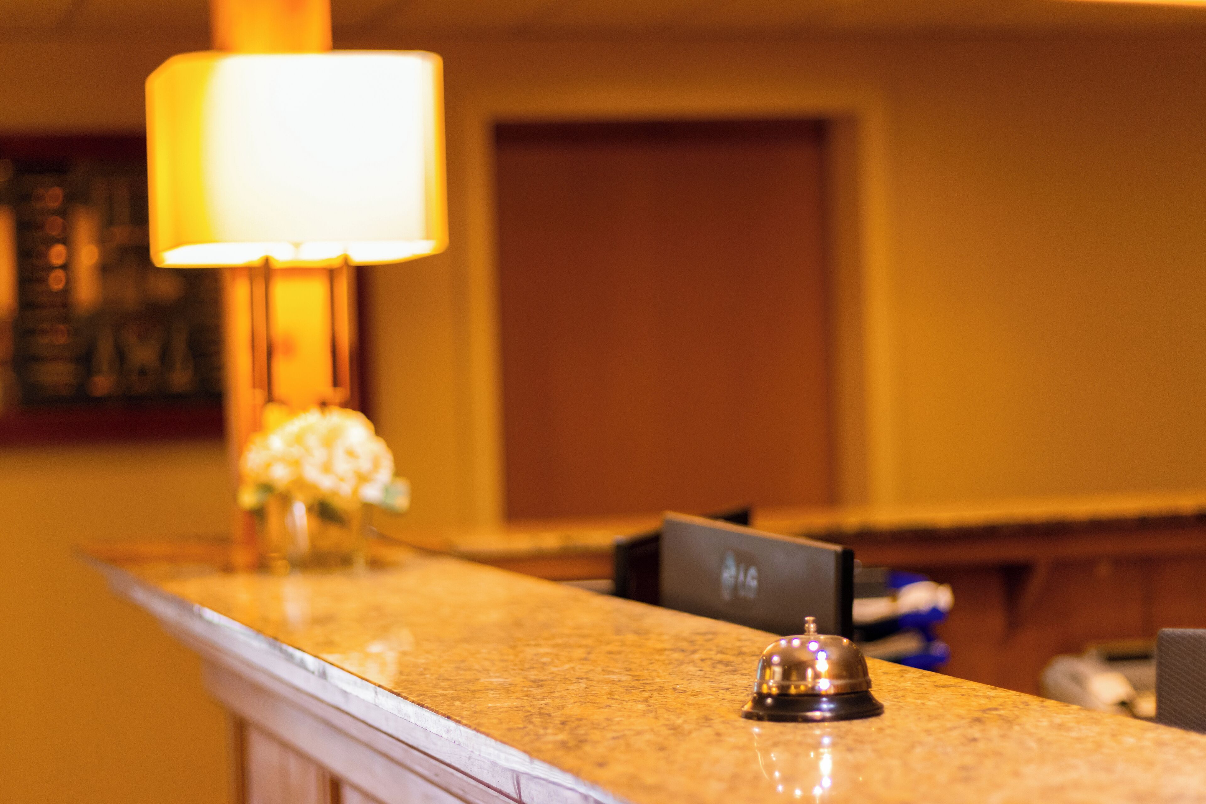 Ein Hotelrezeptionstresen mit Marmorplatte, eine Klingel, eine Lampe und eine Tür im Hintergrund.