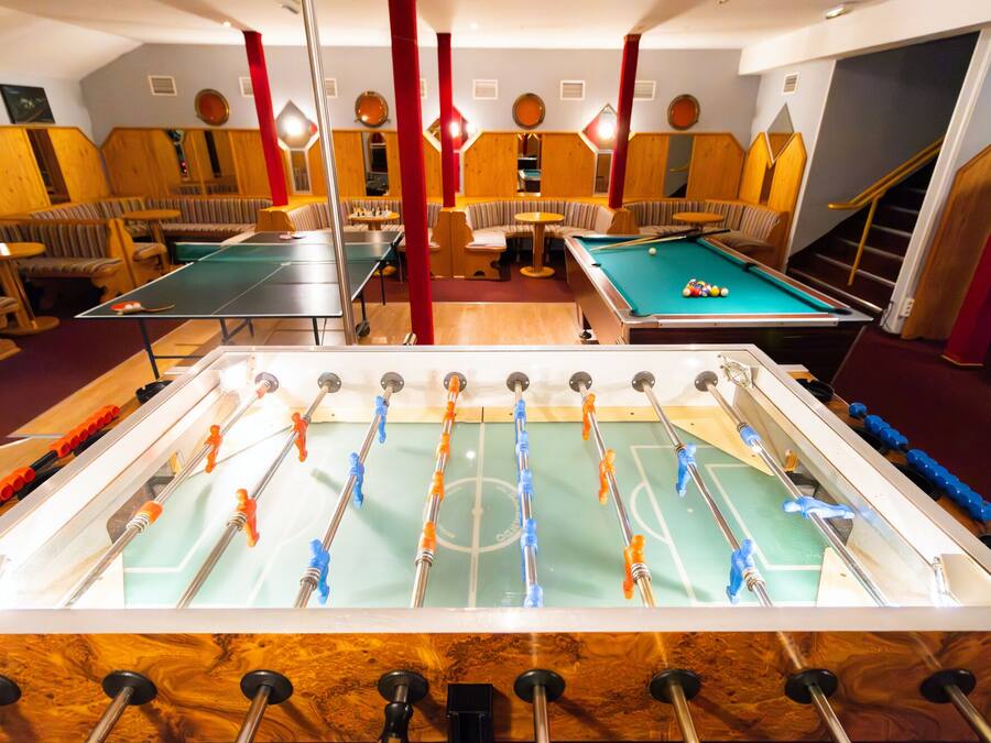 A room with a foosball table, pool table, and seating area with wooden panels and red accents.