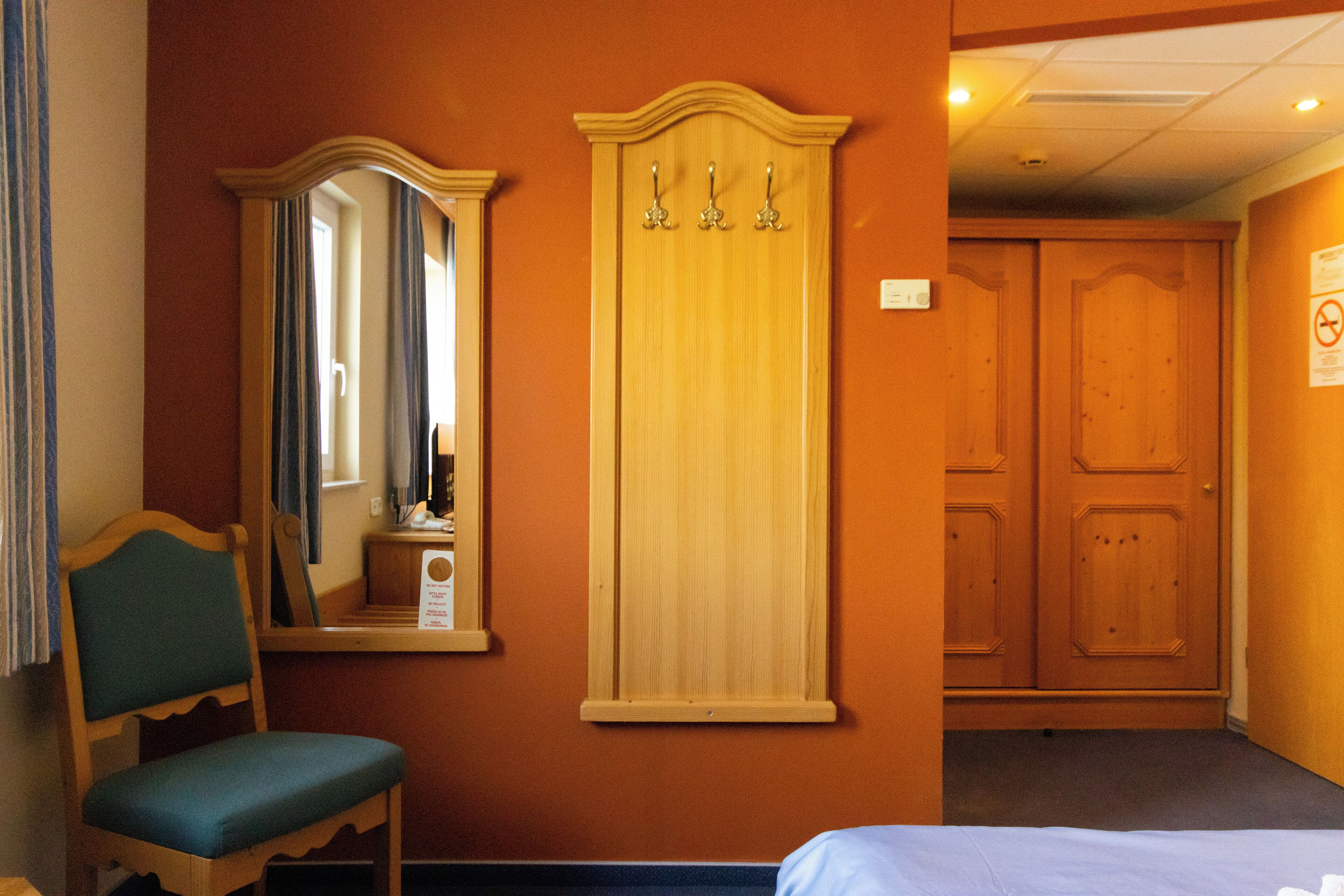 Una habitación de hotel con un armario de madera, un espejo, una silla y una cama.