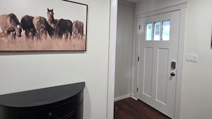 Een gang met een zwarte entertainmentkast, een lijst met paarden en een witte deur met drie ramen.