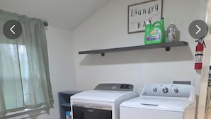 Een wasserette met een wasmachine, droger en een plank met schoonmaakmiddelen.