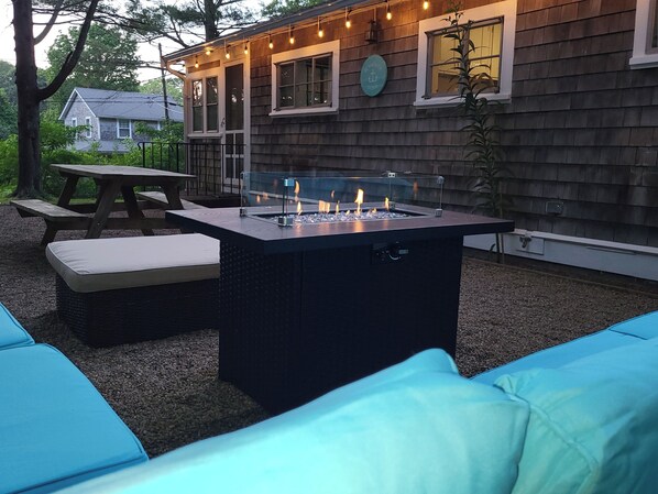 An outdoor patio with a rectangular fire pit, a picnic table, and a cushioned seating area.